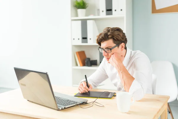 Business, design and people concept - Handsome young man in white shirt using graphic tablet at wooden table