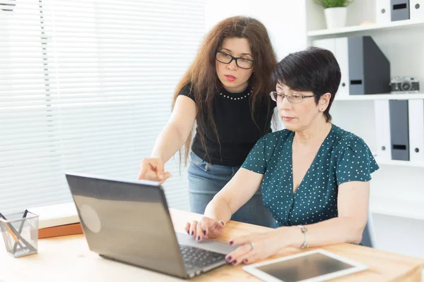 Geschäftsleute, Technologie und Kommunikationskonzept - Frau mittleren Alters zeigt einer anderen Frau am Laptop im Büro etwas — Stockfoto