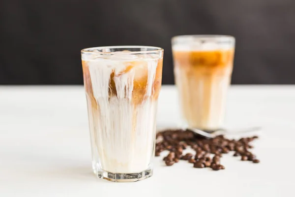Is kaffe i ett glas med grädde över och kaffebönor på bordet — Stockfoto