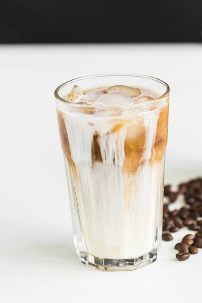 Buzlu kahve bir bardak krem üzerinde ve masanın üzerine kahve çekirdekleri ile — Stok fotoğraf