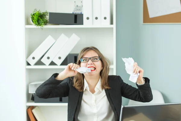 Stres, úřad a lidé koncept - žena, pracovník se spoustou práce u stolu v kanceláři, trhání papíru zuby — Stock fotografie