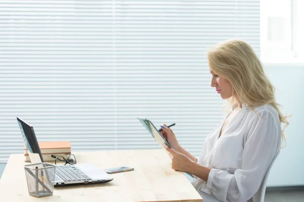 Concepto de tecnología, negocios y personas - Hermosa mujer en gafas trabajando en el ordenador y tomando notas — Foto de Stock