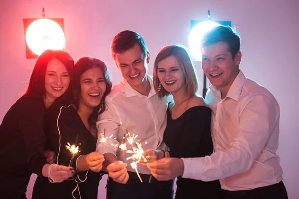 Fiesta de año nuevo, la celebración y el concepto de días festivos - Jóvenes hombres y mujeres alegres celebración de bengalas ardientes —  Fotos de Stock