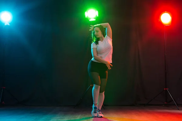 Modern dance, sport and people concept - young woman dancing jazz funk in the darkness under colourful light