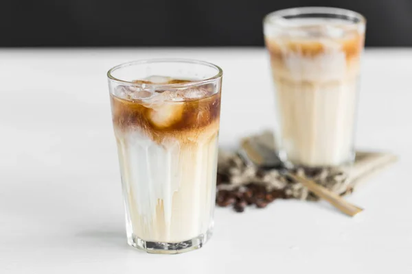 Café gelado em um copo com creme sobre e grãos de café na mesa — Fotografia de Stock