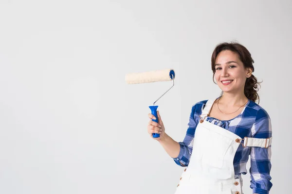 Repair, renovation, new home and people concept - young woman doing redecoration and show us thumbs up over white wall with copy space — Stock Photo, Image