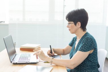 Office, grafik tasarımcı, dijital - dizüstü bilgisayar ve dijital tablet ofisinde çalışan orta yaş kadın