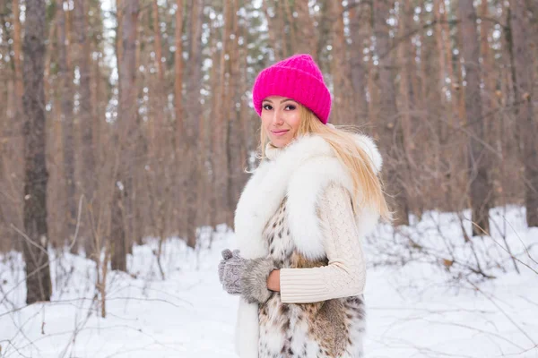 Mode, saison et concept de personnes - Bonne femme blonde avec un chapeau rose et des gants et un pull dans la forêt d'hiver sourit — Photo