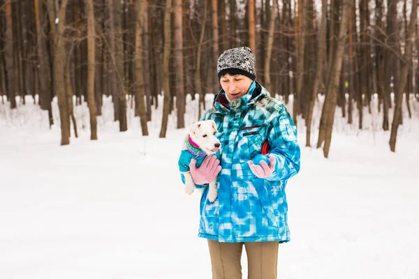 Dono de animais de estimação e conceito de inverno - Mulher de meia-idade brincando com seu cão terrier jack russell no parque nevado . — Fotografia de Stock