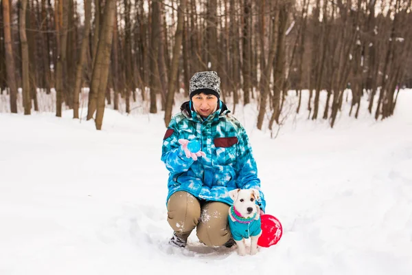 Dono de animais de estimação e conceito de inverno - Mulher de meia-idade brincando com seu cão terrier jack russell no parque nevado . — Fotografia de Stock