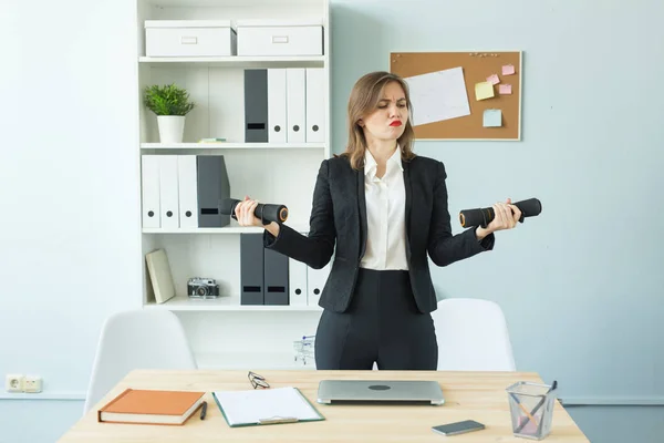 Business, fitness in office and people concept - Satisfied woman in office holding dumbbell in hand