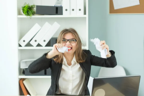 Stres, úřad a lidé koncept - žena, pracovník se spoustou práce u stolu v kanceláři, trhání papíru zuby — Stock fotografie