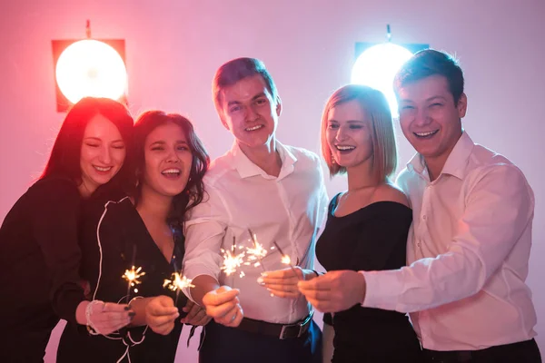 New year party, celebration and holidays concept - Young cheerful men and women holding burning sparklers — Stock Photo, Image