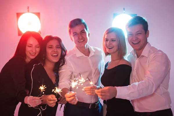 Fiesta de año nuevo, la celebración y el concepto de días festivos - Jóvenes hombres y mujeres alegres celebración de bengalas ardientes —  Fotos de Stock