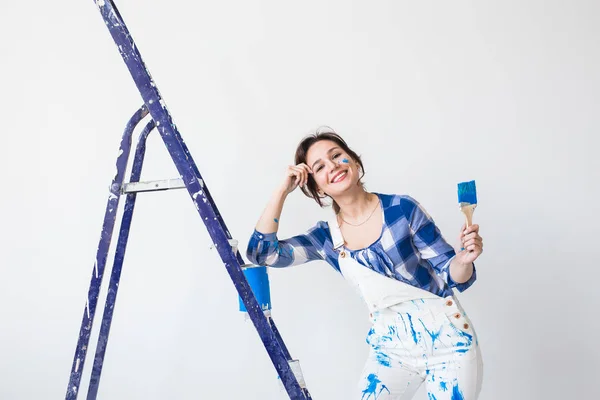 People, renovation and work concept - Beautiful woman standing on the ladder and painting walls — Stock Photo, Image