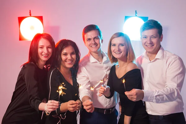 Fiesta de año nuevo, la celebración y el concepto de días festivos - Jóvenes hombres y mujeres alegres celebración de bengalas ardientes —  Fotos de Stock