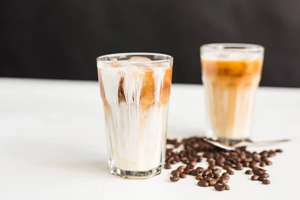 Кофе со льдом в стакане со сливками и кофейными зернами на столе — стоковое фото