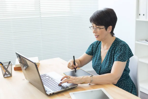 Büro, Grafikdesignerin, digital - Frau mittleren Alters im Büro mit Laptop und digitalem Tablet — Stockfoto