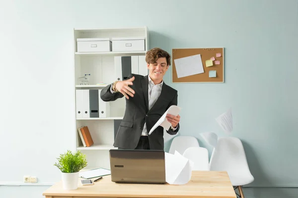 Podnikání, humor a lidi koncept - krásný a mladý muž v obleku vyvolá listů papíru v kanceláři — Stock fotografie