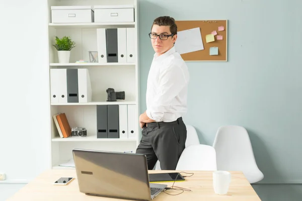 Business, office, people concept - Handsome man in glasses stands in the office near a computer and smiling — Stock Photo, Image