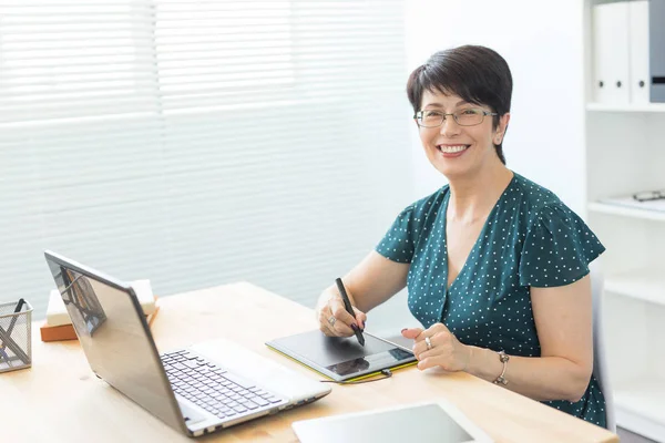 Büro, Grafikdesignerin, digital - Frau mittleren Alters im Büro mit Laptop und digitalem Tablet — Stockfoto