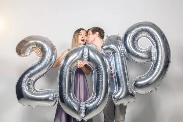 Πρωτοχρονιά, γιορτή και έννοιας διακοπές - αστεία αστεία αγάπη ζευγάρι κρατώντας υπογράφουν 2019 κατασκευασμένα από ασήμι μπαλόνια για το νέο έτος σε λευκό φόντο — Φωτογραφία Αρχείου