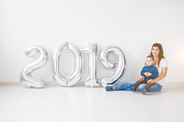 New 2019 Year is coming concept - Mother with her baby son sitting near silver colored numbers indoors.