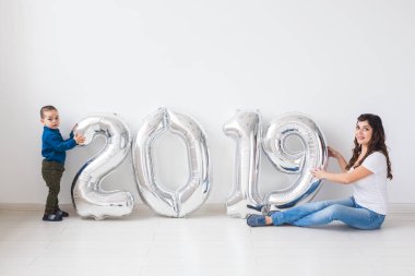 Yeni yıl, kutlama ve tatil kavramı - anne ve oğlu işareti 2019 oturan beyaz Oda arka planda yeni yıl için gümüş balon yaptı