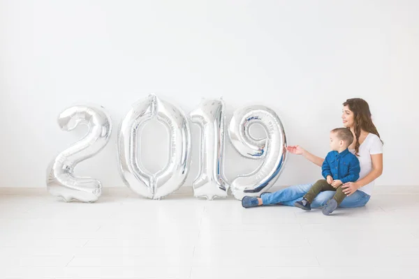 Nuevo 2019 Año viene concepto - Madre con su hijo pequeño sentado cerca de números de color plata en el interior . — Foto de Stock