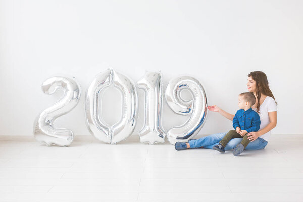 New 2019 Year is coming concept - Mother with her baby son sitting near silver colored numbers indoors.