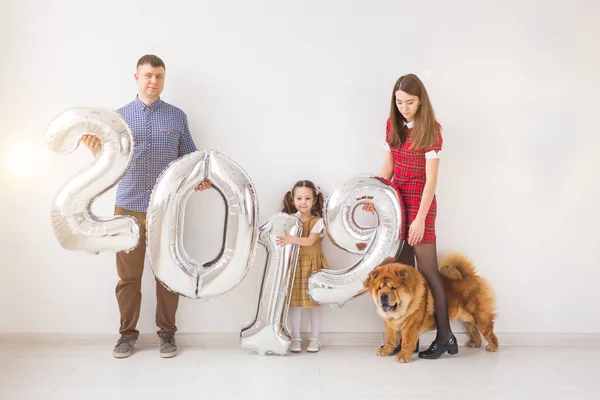 Nuevo 2019 Año viene concepto - Alegre madre, padre, hija y perro están sosteniendo números de color plata en el interior . — Foto de Stock