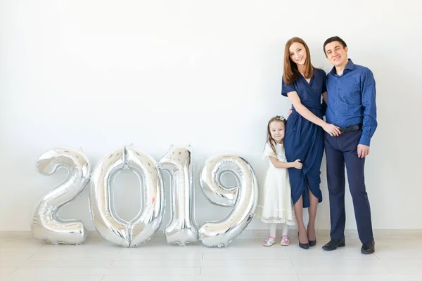 Año nuevo, celebración y concepto de vacaciones - familia de pie cerca de signo 2019 hecho de globos de plata para el año nuevo en el fondo de la habitación blanca — Foto de Stock