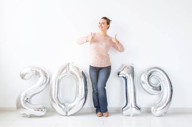 Yeni 2019 yılı önümüzdeki - mutlu kadın gümüş renkli numaraları kapalı başparmak gösterilmesini kavramdır.