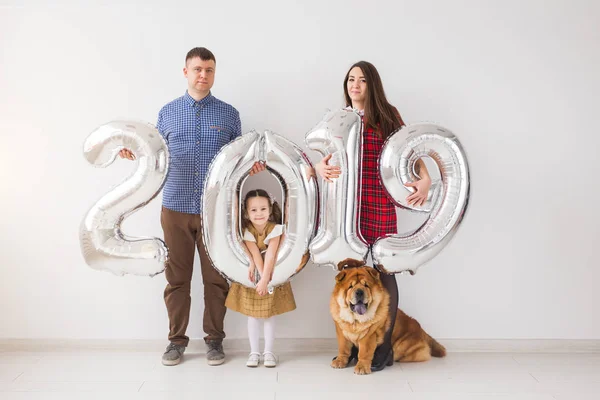 Nuevo 2019 Año viene concepto - Alegre madre, padre, hija y perro están sosteniendo números de color plata en el interior . — Foto de Stock