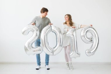 Yeni 2019 yılı önümüzdeki kavramı - mutlu genç adam ve kadın beyaz arka plan üzerinde gümüş renkli numaraları tutuyorsun
