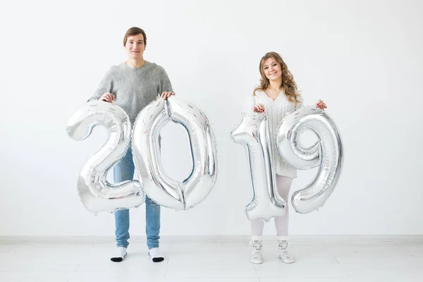 Nuevo 2019 Año viene concepto - Alegre joven hombre y mujer están sosteniendo números de color plata — Foto de Stock