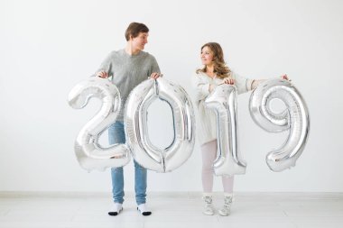 Yeni 2019 yılı önümüzdeki kavramı - komik genç adam ve kadın beyaz arka plan üzerinde gümüş renkli numaraları tutuyorsun