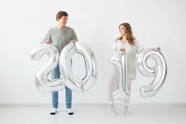 Nuevo 2019 Año viene concepto - Feliz joven hombre y mujer están sosteniendo números de color plata sobre fondo blanco — Foto de Stock