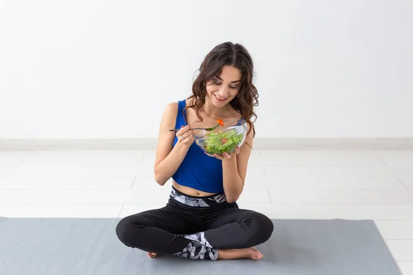 Υγιεινού τρόπου ζωής, άνθρωποι και sport concept - γιόγκα γυναίκα με ένα μπολ σαλάτα λαχανικών μετά την εκπαίδευση πάνω από το λευκό φόντο — Φωτογραφία Αρχείου