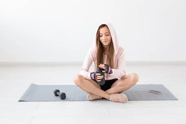 Estilo de vida saludable, personas y concepto deportivo - Mujer sentada en una esterilla de yoga y bebiendo agua después de un duro entrenamiento — Foto de Stock