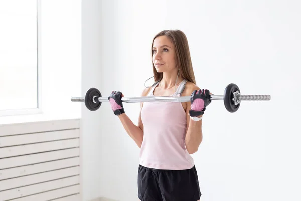 Sport, fitness e concetto di persone - Adatta agli esercizi di una giovane donna con una barra del peso, facendo i suoi bicipiti — Foto Stock