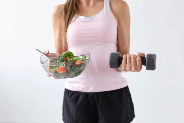 Dieta, jídlo a fitness koncept - Zavřít se zdravého salátu a činka v ženské ruce nad bílým pozadím — Stock fotografie
