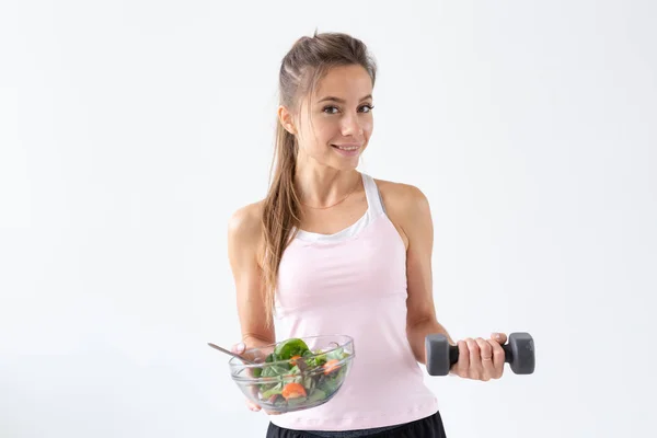 Mode de vie sain, régime alimentaire, fitness et concept de personnes - jeune femme mange une salade et fait du sport avec haltère sur fond blanc avec espace de copie — Photo