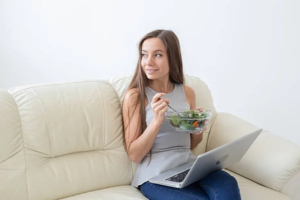 Mode de vie sain, bonne alimentation, se détendre et les gens concept- jeune belle femme assise sur le canapé blanc et de manger une salade — Photo