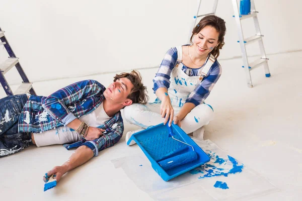 Sonriente pareja amorosa haciendo renovaciones en casa. Mujer joven sostiene un rodillo de pintura y hombre joven está descansando — Foto de Stock