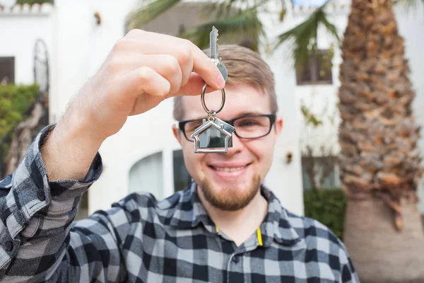 Feliz dueño de la casa. Sonriente joven sosteniendo las teclas y mirando a la cámara mientras está de pie contra el nuevo fondo del hogar —  Fotos de Stock