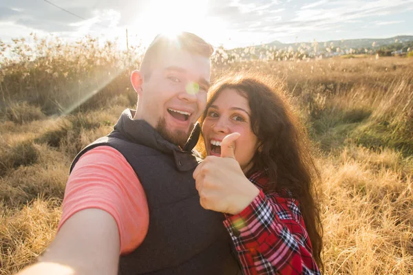 Reise, Tourismus und Naturkonzept - lächelndes Paar macht Selfie auf dem Feld und zeigt Daumen hoch — Stockfoto