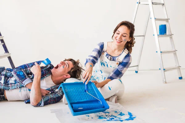 Couple aimant souriant faisant des rénovations de maison. Jeune femme tient un rouleau de peinture et jeune homme se repose — Photo