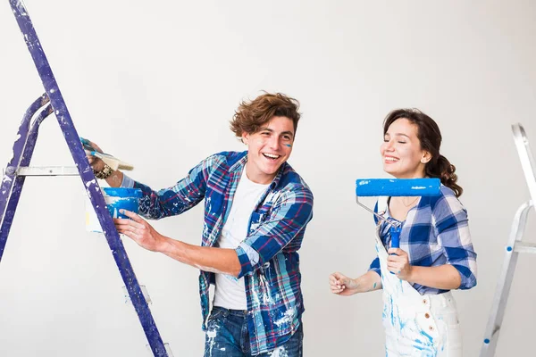 Ремонт, ремонт и любовь пара концепции - молодая семья делает ремонт и покраска стен вместе и смех . — стоковое фото