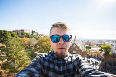 Seyahat ve tatil kavramı - yakışıklı adam akıllı telefon Park Guell, Barselona, İspanya, gülümseyen ile kamera çekimi fotoğrafa bakan.
